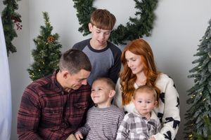 Family of five posing for a Christmas portrait with holiday greenery and trees in the background.