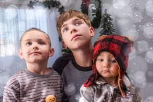 Three children looking up in wonder near a Christmas tree with festive snow effect backdrop.