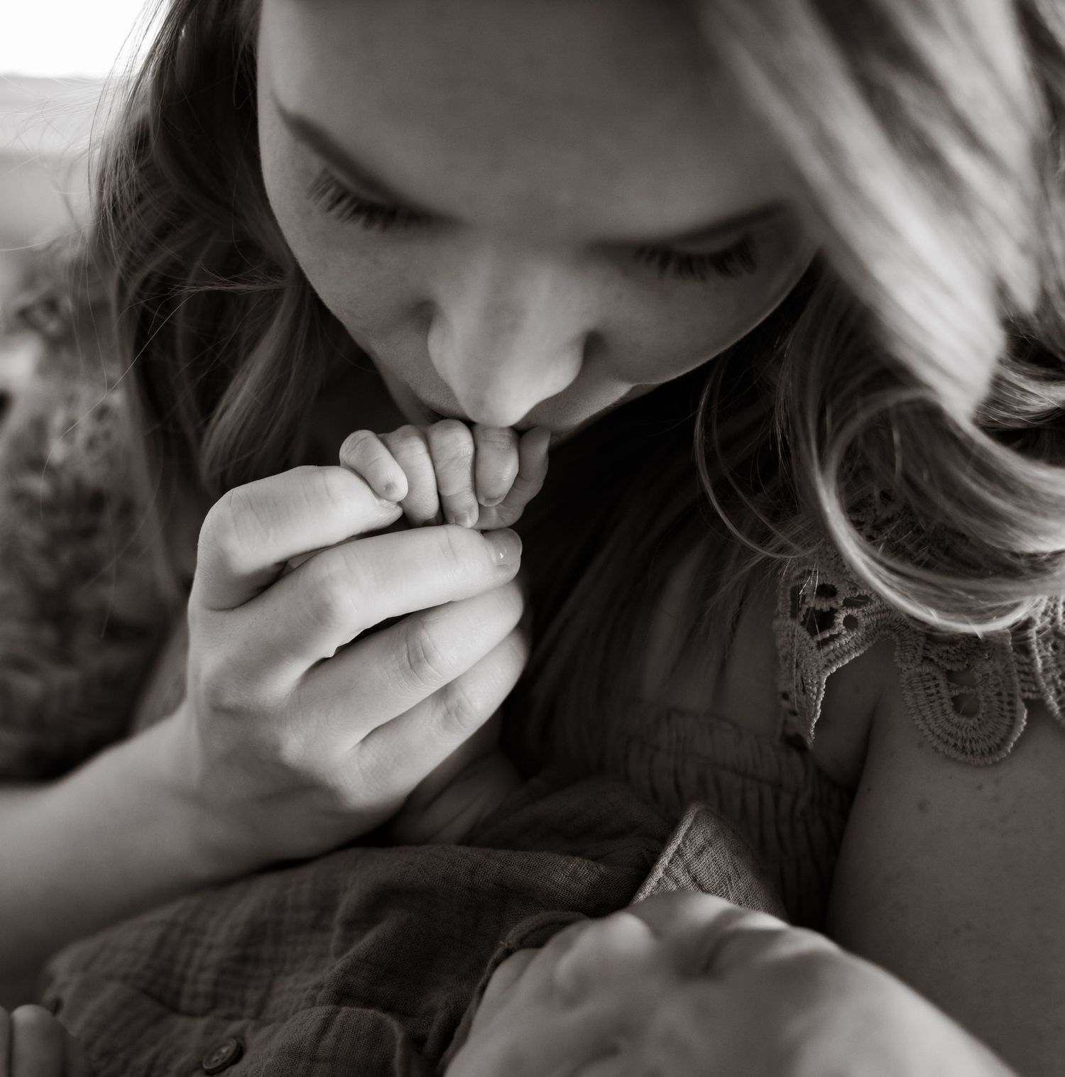 black and white photo of mother tenderly kissing newborn hand