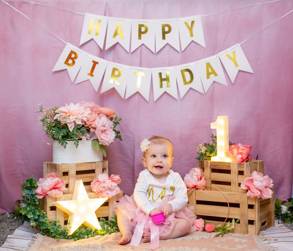 Pink and white birthday setup with wooden crates, floral arrangements and a sparkly gold star light on pink backdrop.