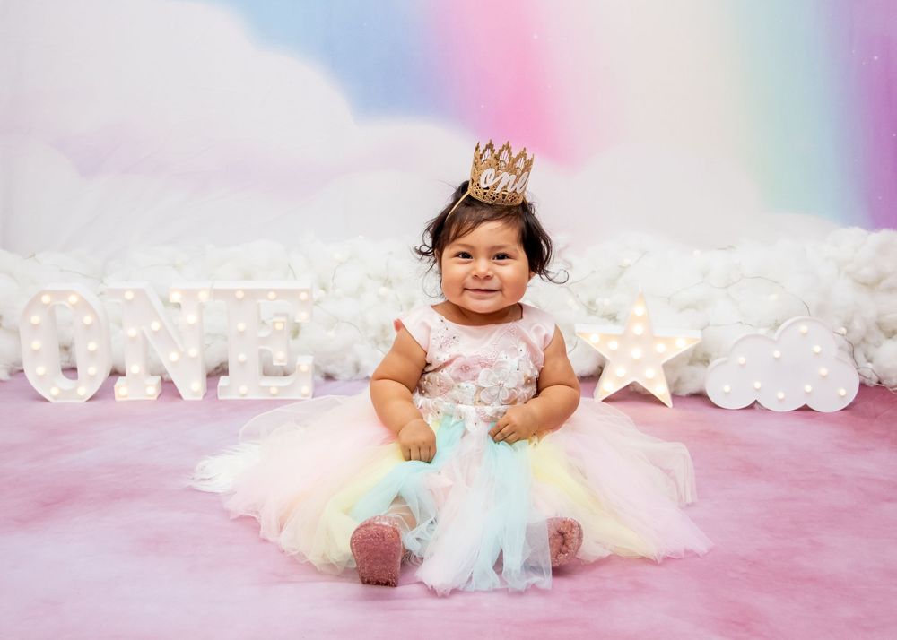 Baby seated on pink background surrounded by tulle fabric and twinkling lights creating a dreamy atmosphere.