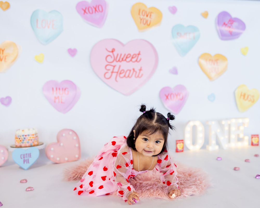 Sweet Valentine's day photo backdrop with conversation hearts and pink decorative elements for a first birthday celebration.