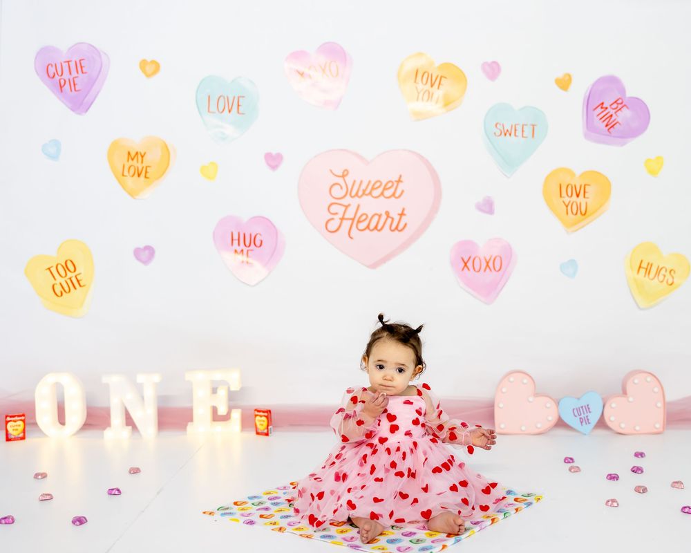 Valentine's themed first birthday setup with pink decor, confetti, light-up ONE letters and heart wall decorations.