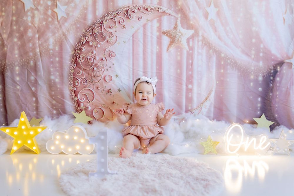 Dreamy pink nursery setup with decorative crescent moon prop, fluffy white clouds, and glowing star lights.