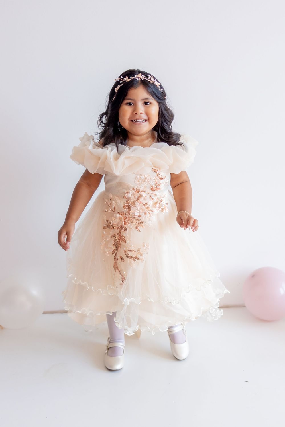 Three photos of a smiling toddler wearing a delicate peach-colored lace dress with floral details and white shoes.