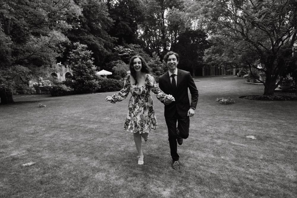 Couple runs joyfully across a lush garden lawn in black and white.