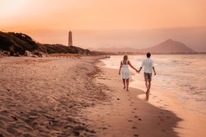 Couple walking along a Mallorca beach at sunset during a romantic engagement photoshoot.