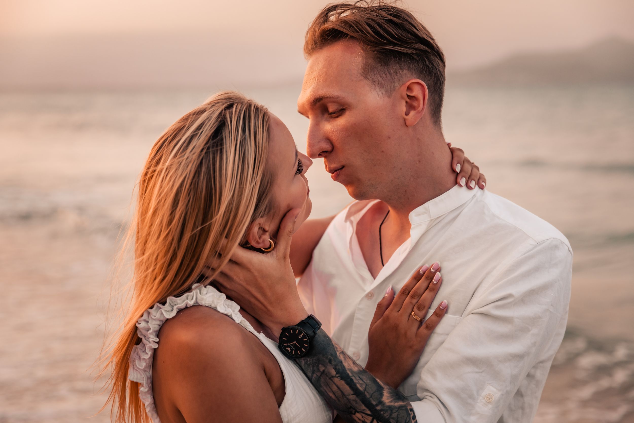 Close-up portrait of a couple embracing on a beach with a blurred ocean background.