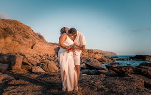 Romantic couple embracing on rocky coastline during a sunset engagement photoshoot in Mallorca.