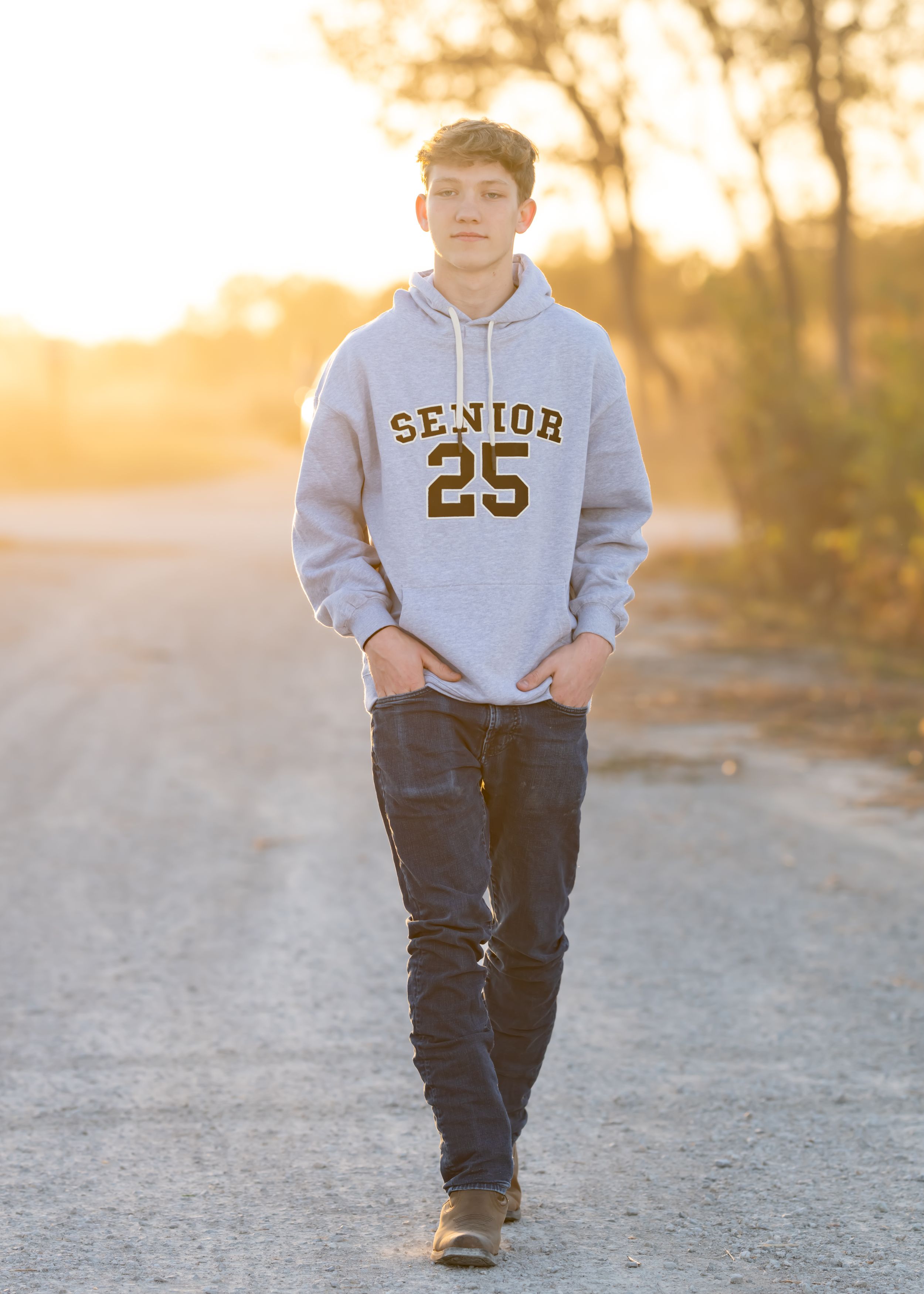 Person walks on dirt path wearing Senior 25 sweatshirt at sunset.