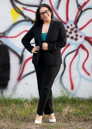 Professional wearing black suit and teal top poses in front of colorful floral wall art.