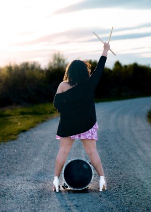 Playful pose with drumsticks over tire on country road at sunset.