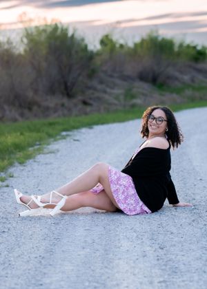 Casual portrait of woman in black top and floral skirt relaxing on gravel path.
