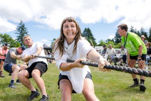 People participate in an outdoor field game competition on a sunny summer day with trees in background.