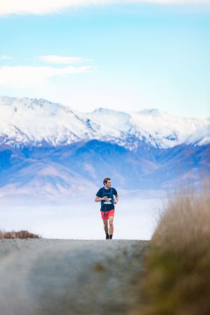 Solo runner against dramatic mountain landscape with snow-capped peaks and morning fog.