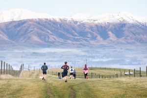 Runners training on a scenic mountain trail with snow-capped peaks and valley fog in the background.
