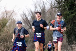 Three runners enjoying a trail run through wooded area during a race event.