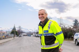 Police officer in high-visibility vest smiling on patrol with mountain backdrop.