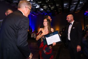 People interact during an awards ceremony in a dimly lit venue with blue accent lighting and formal attire.