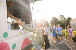 Cheerful customers line up at a colorful food truck during a sunny summer evening.