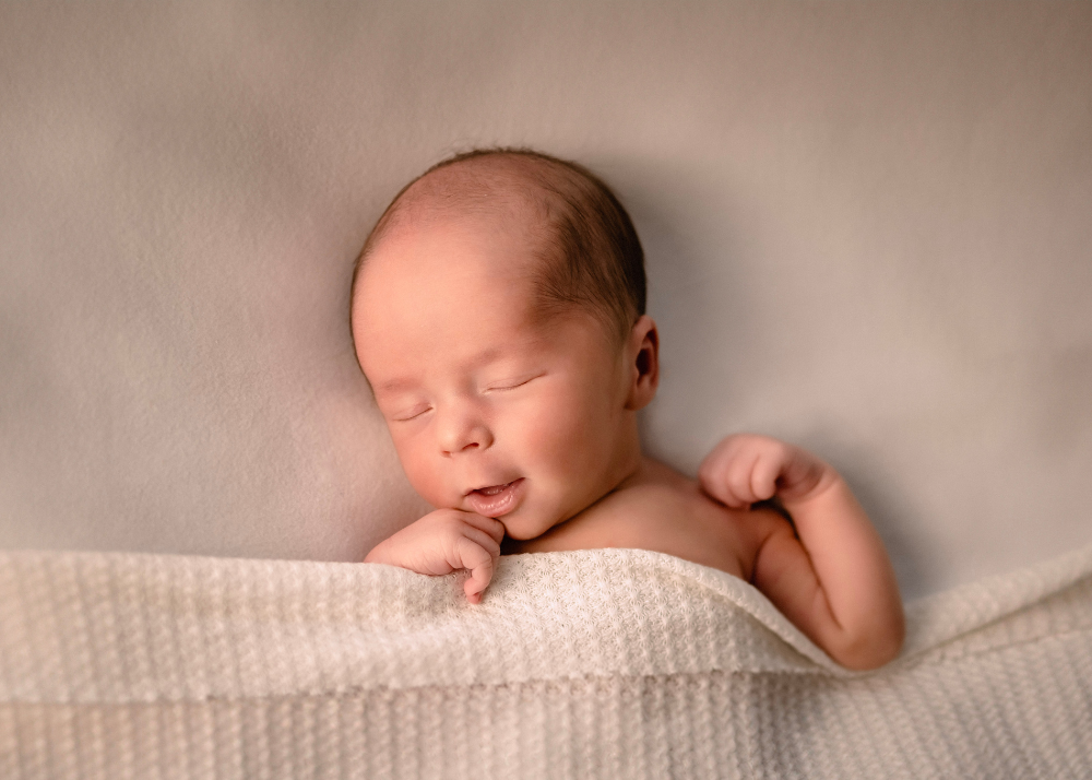 Peaceful sleeping newborn baby wrapped in soft white textured blanket during professional portrait session.