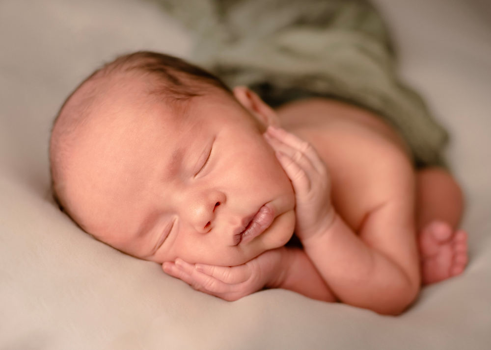 Peaceful sleeping newborn with hands softly resting near face on white blanket.