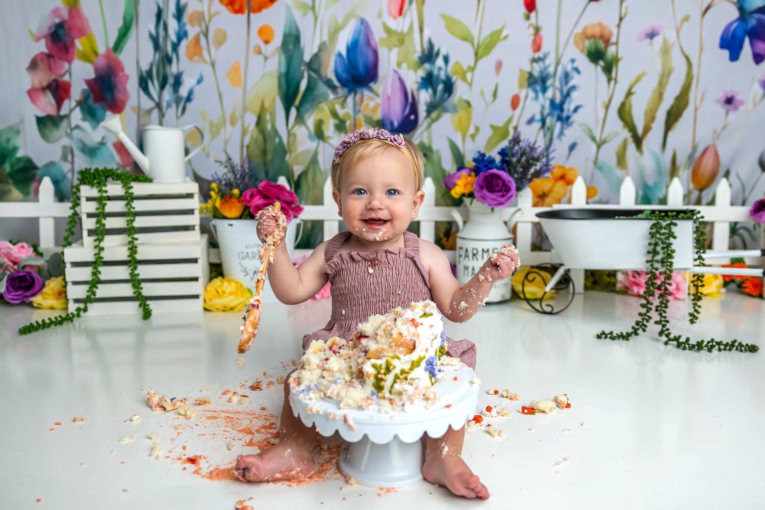 Colorful floral backdrop cake smash photography session with white cake on decorative stand.