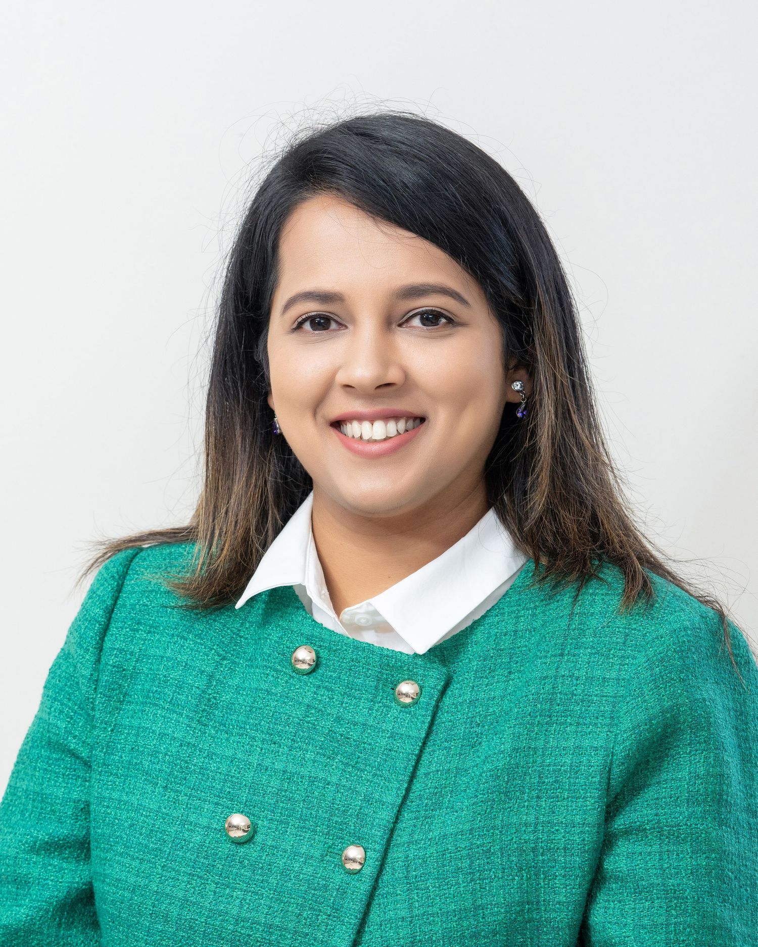 Professional headshot wearing green textured jacket with white collar against light background.