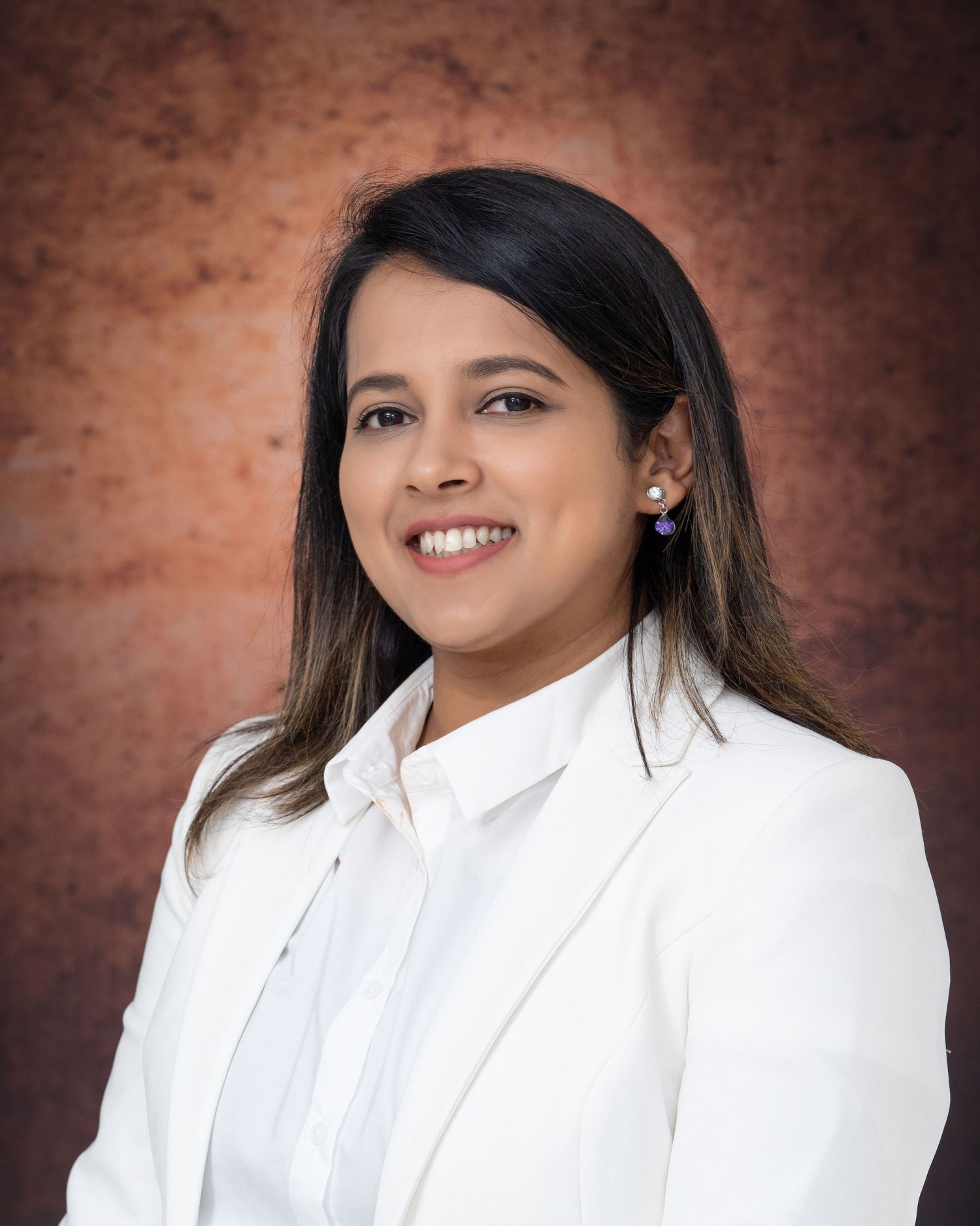 Professional portrait in white blazer and shirt against textured brown background.