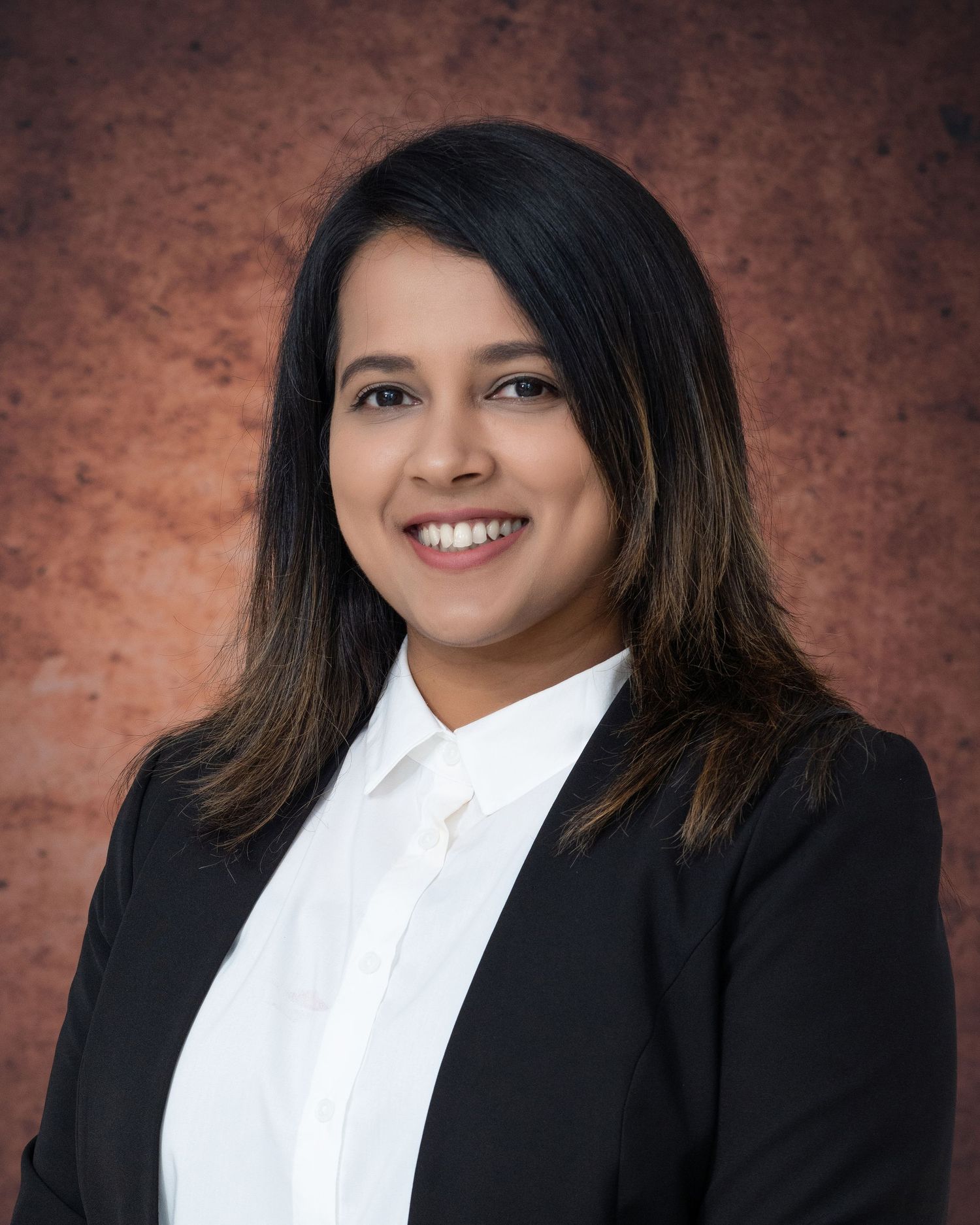 Business portrait in black blazer and white shirt against brown textured backdrop.