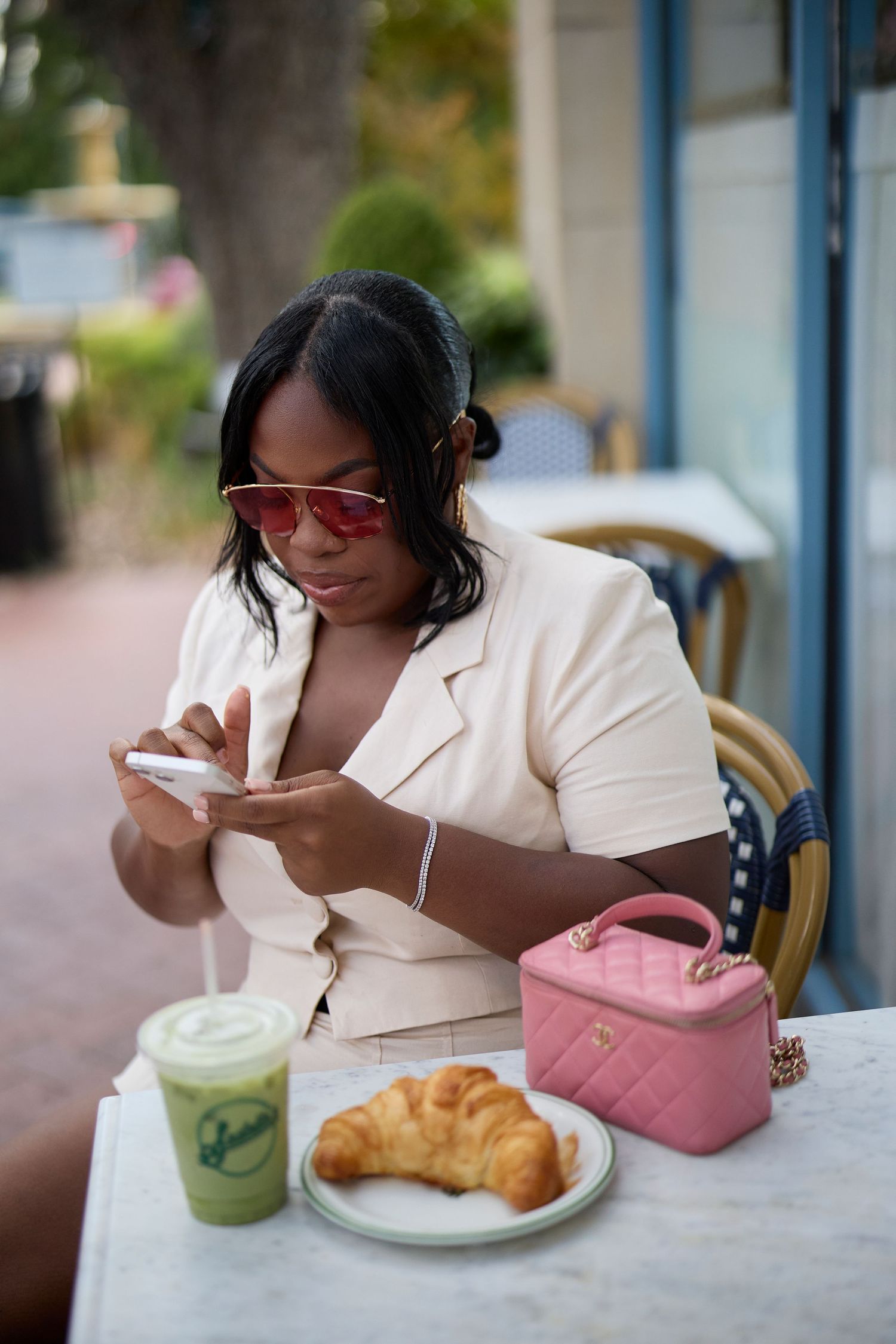 Person enjoying breakfast with a croissant and beverage at an outdoor cafe table. Crystal Chanel