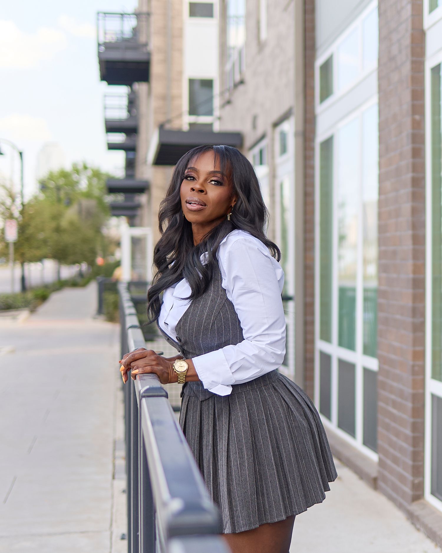 Street style fashion photo in pleated grey dress and white shirt against urban backdrop. Nedra Monet