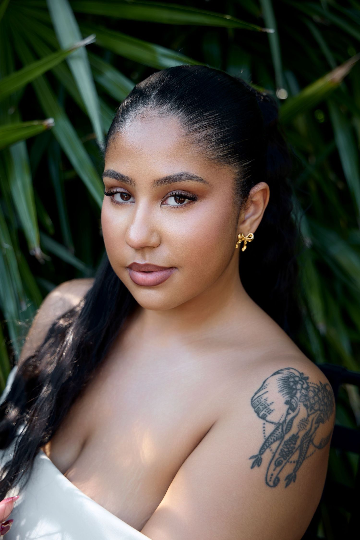 Beauty portrait with visible shoulder tattoo against tropical foliage background.