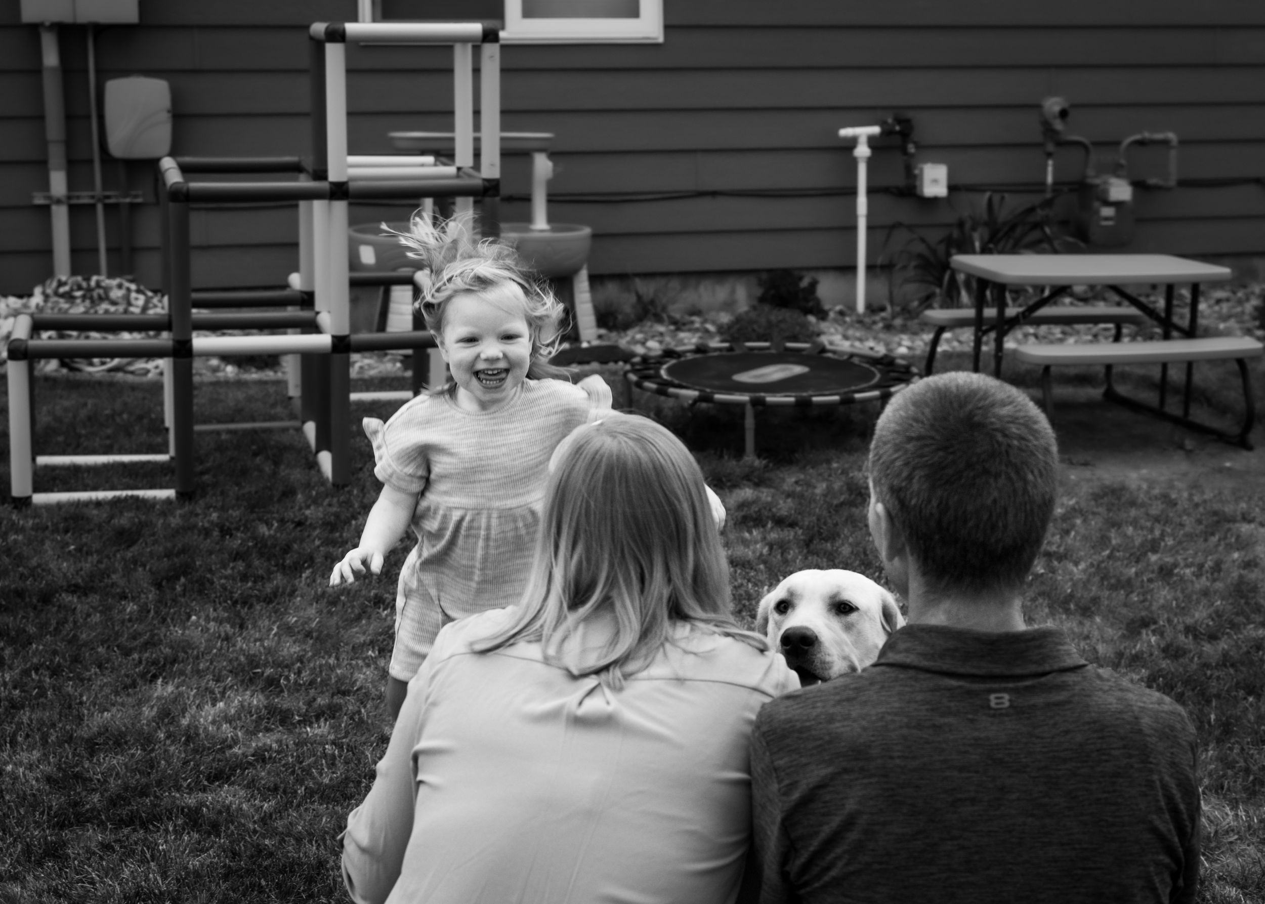 Black and white photo Fort Benton family photography Chouteau County with pup in own backyard, personalized photoshoot genuine smiles