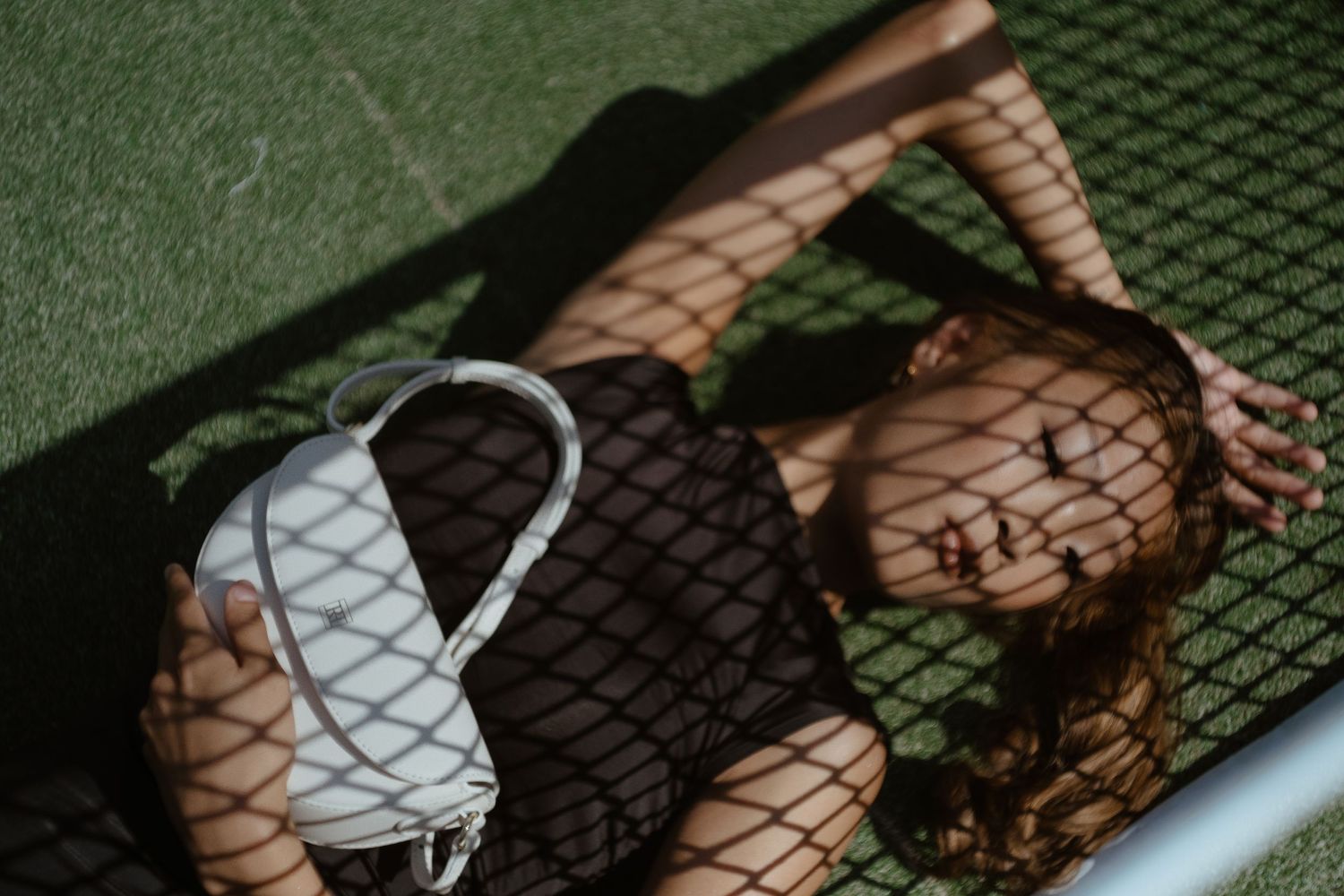 a model lying in a tennis court holding a white bag while being captured by lifestyle photographer in Stockholm