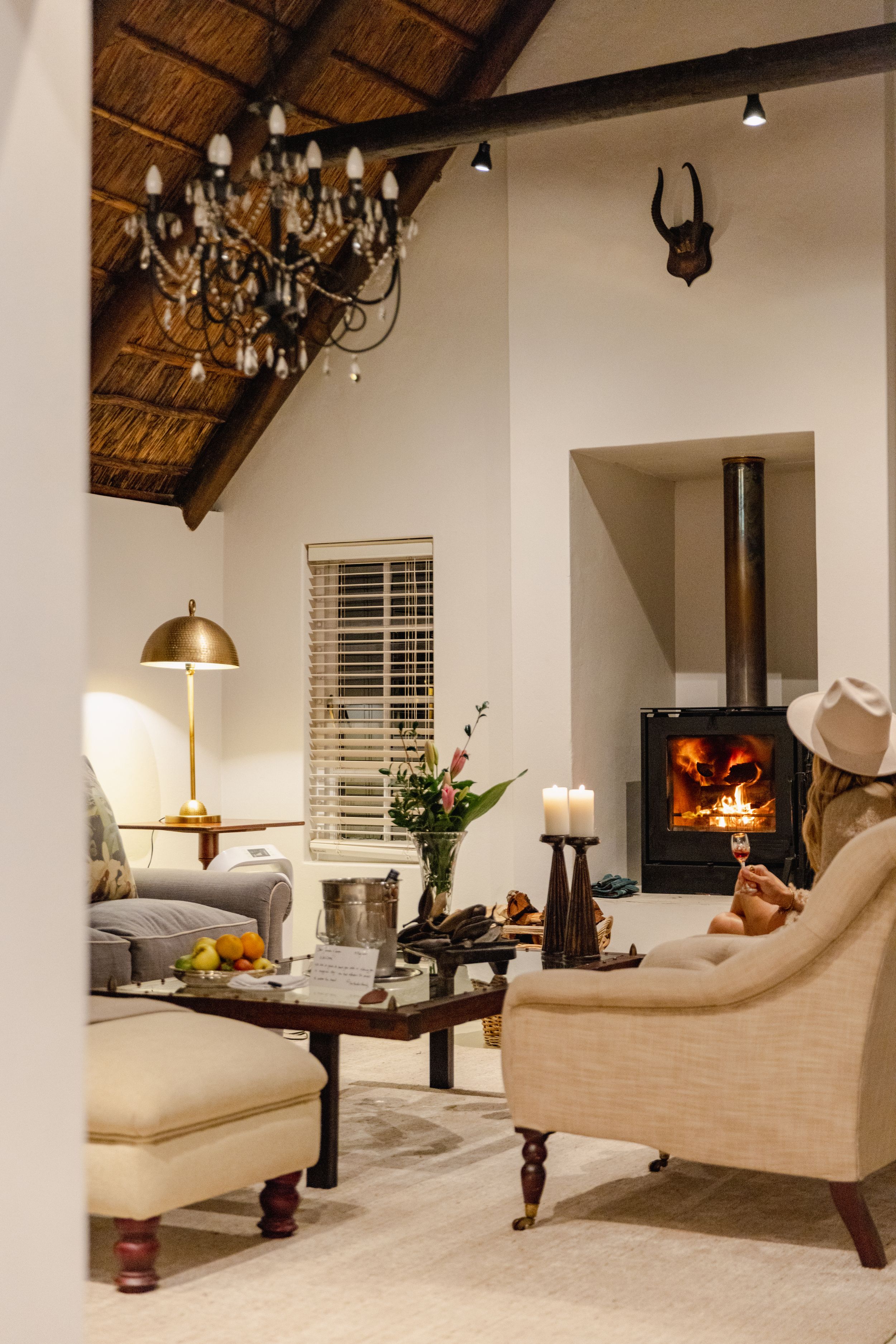 Cozy living room with thatched ceiling, chandelier, and wood-burning stove creating warm ambiance.