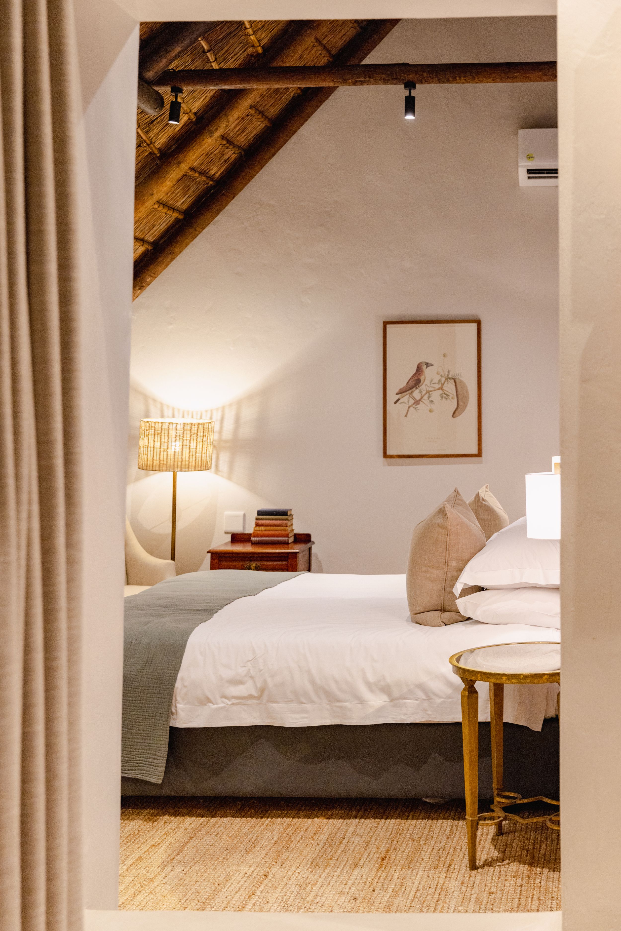 Rustic bedroom interior with exposed beams, white bedding, and bird artwork on the wall.