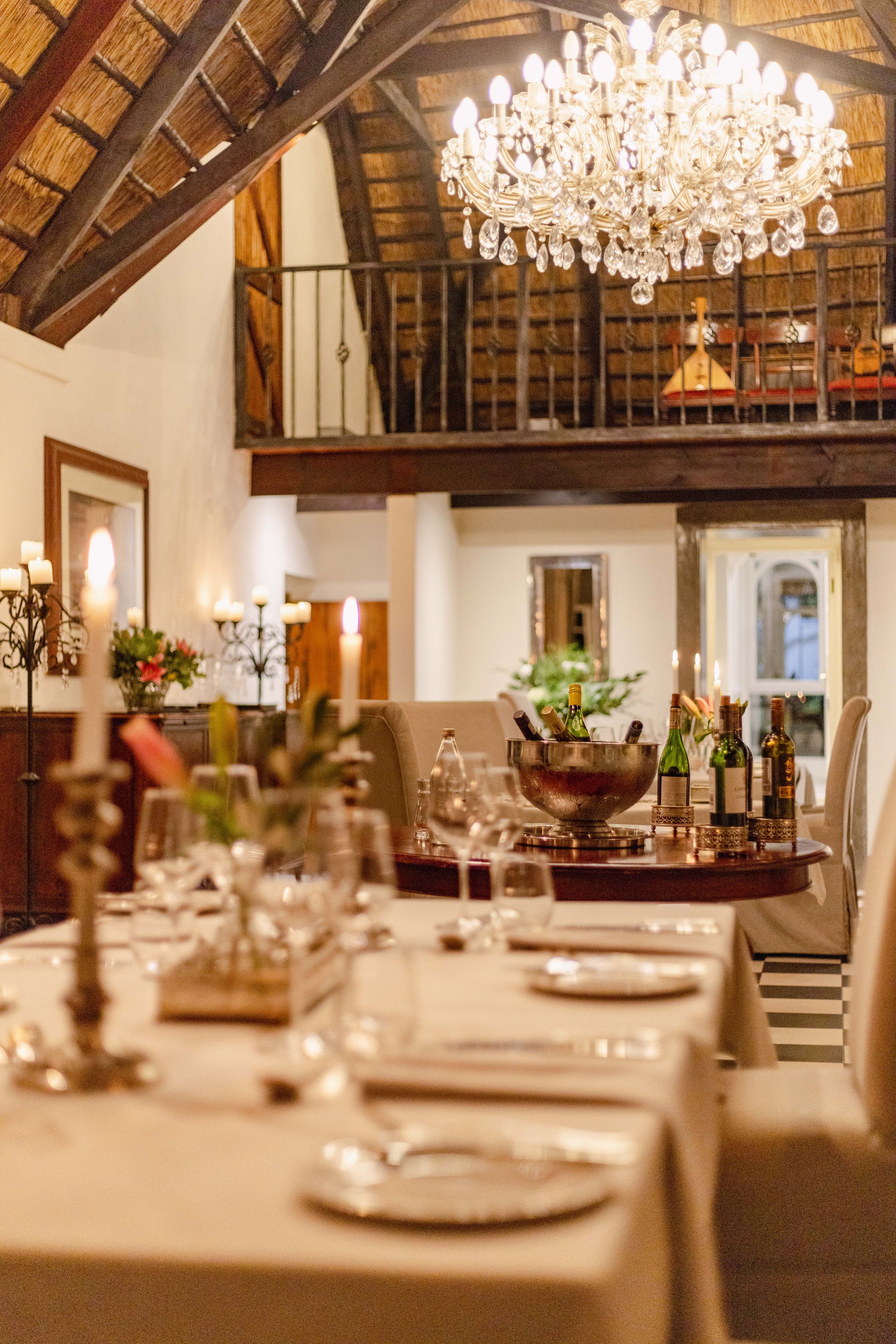 Elegant dining room with crystal chandelier, exposed beams, and formal place settings.