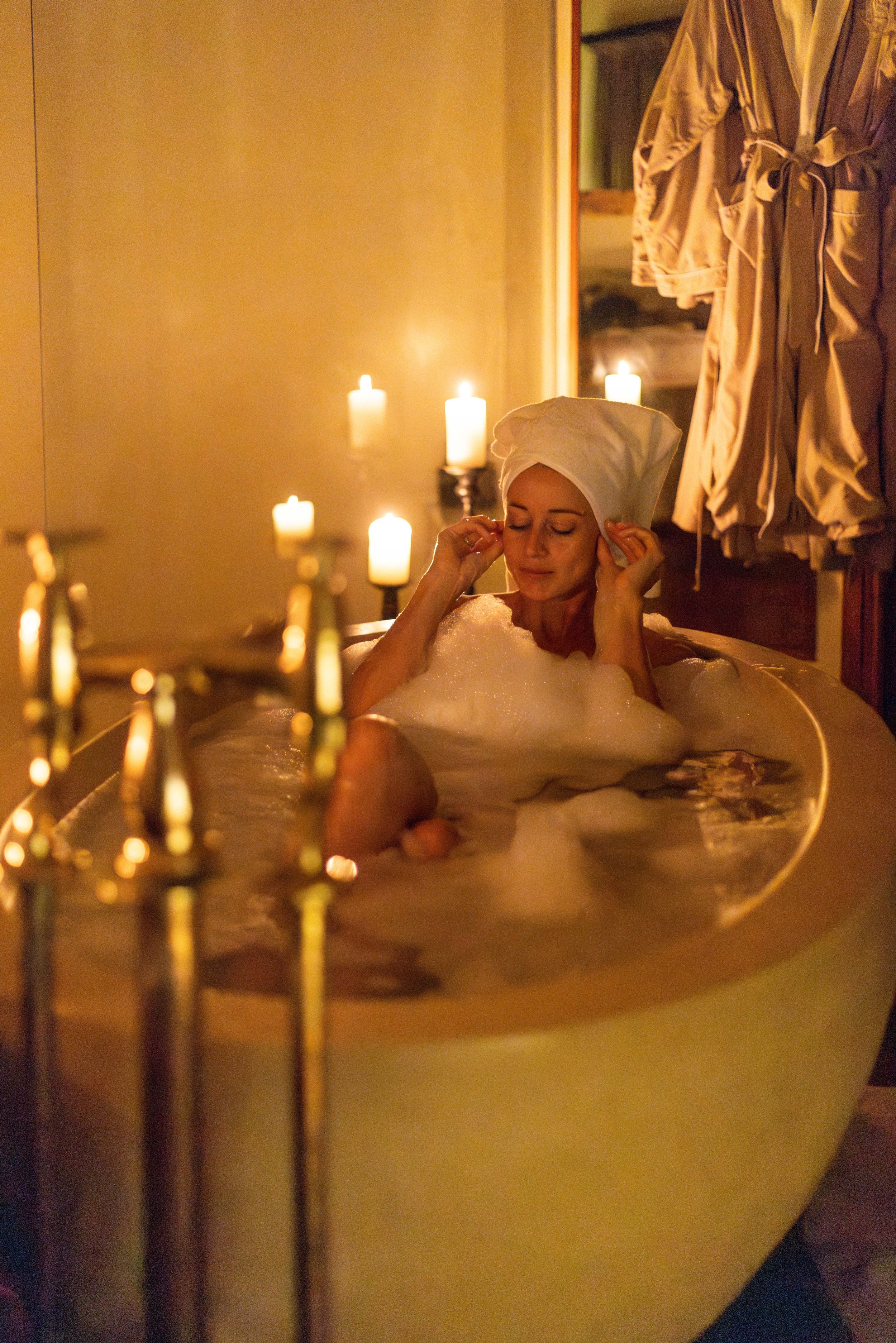 Candlelit bathroom scene with freestanding tub surrounded by glowing candles in warm lighting.