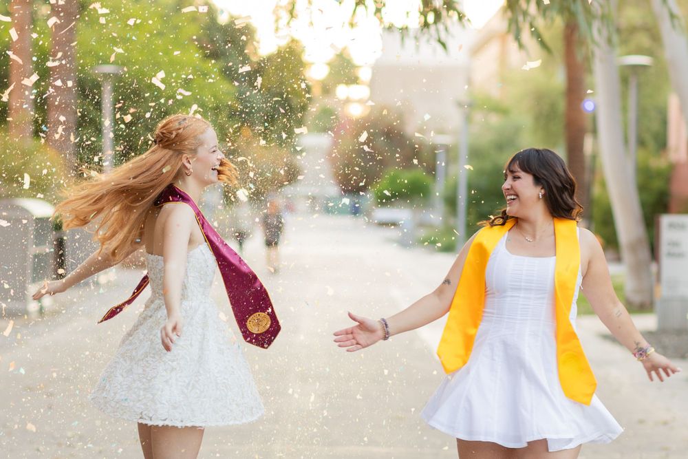 Two people in white dresses with colorful vests dancing and playing with flower petals on a path.
