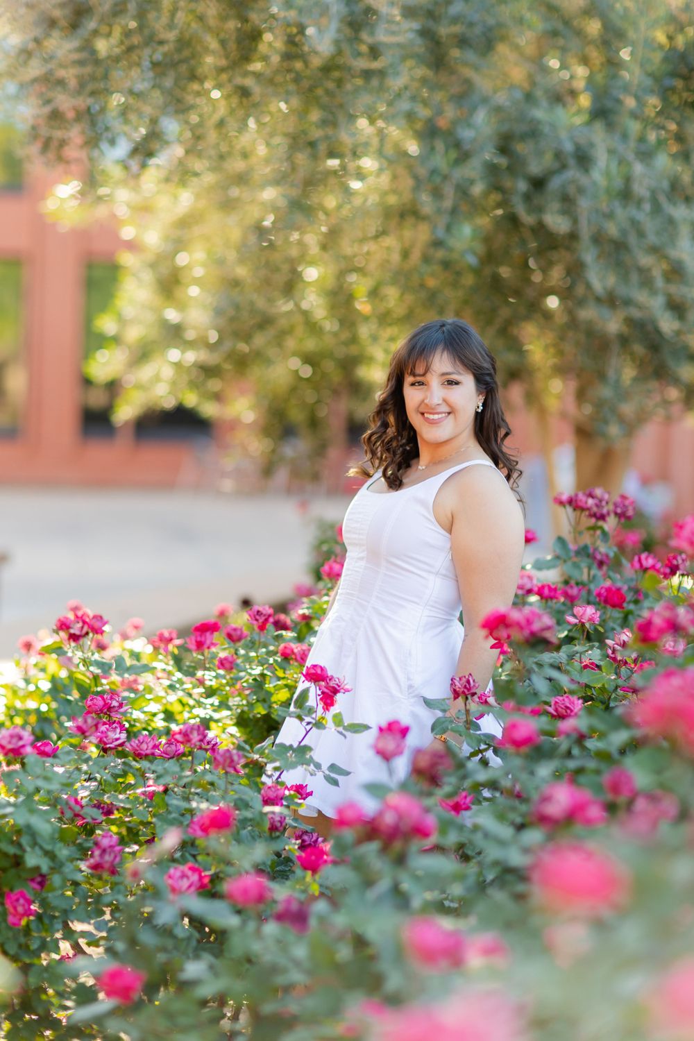 Figure stands gracefully among blooming pink roses wearing a white summer dress.