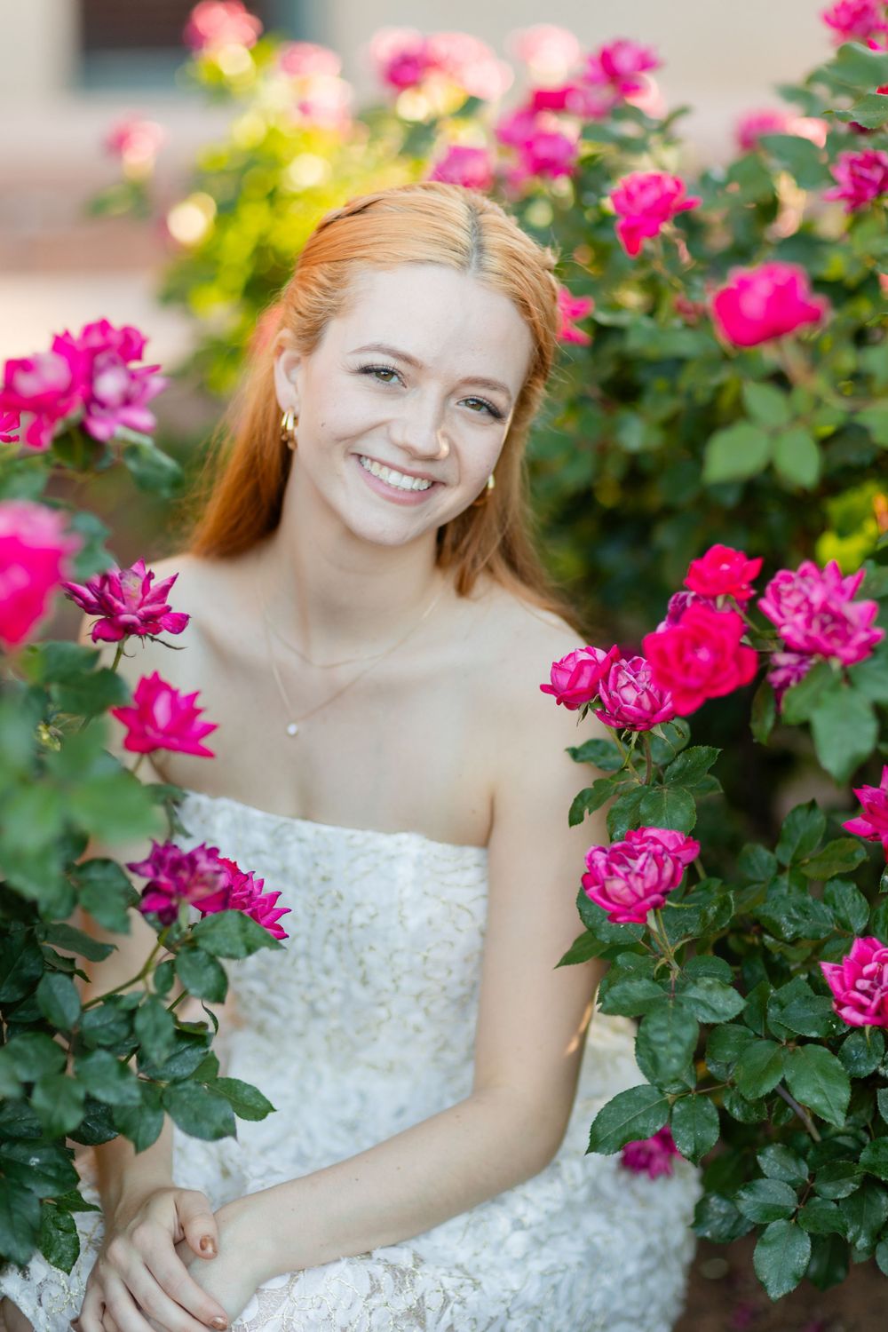Portrait in a rose garden featuring person wearing white dress among pink blooms.