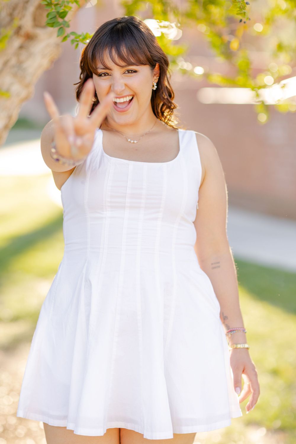 A joyful pose in a white summer dress outdoors with natural bokeh lighting effects in the background.