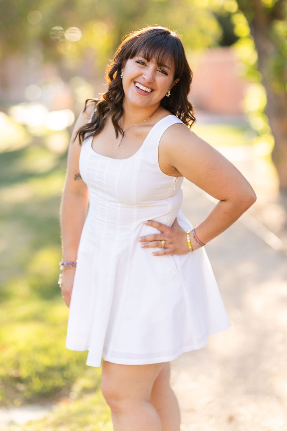 Cheerful outdoor portrait in white sleeveless dress with sunny garden background.