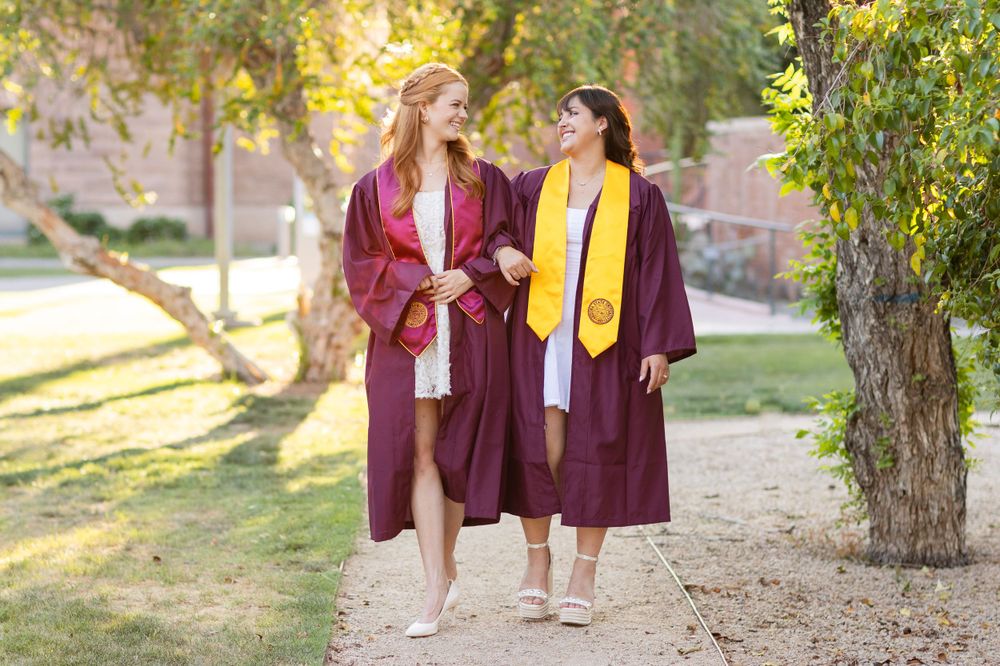Two graduates in maroon caps and gowns walking together outdoors.