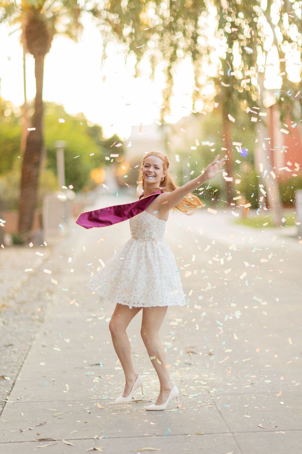 Person in white dress throwing flower petals in golden sunlight with palm trees in background.