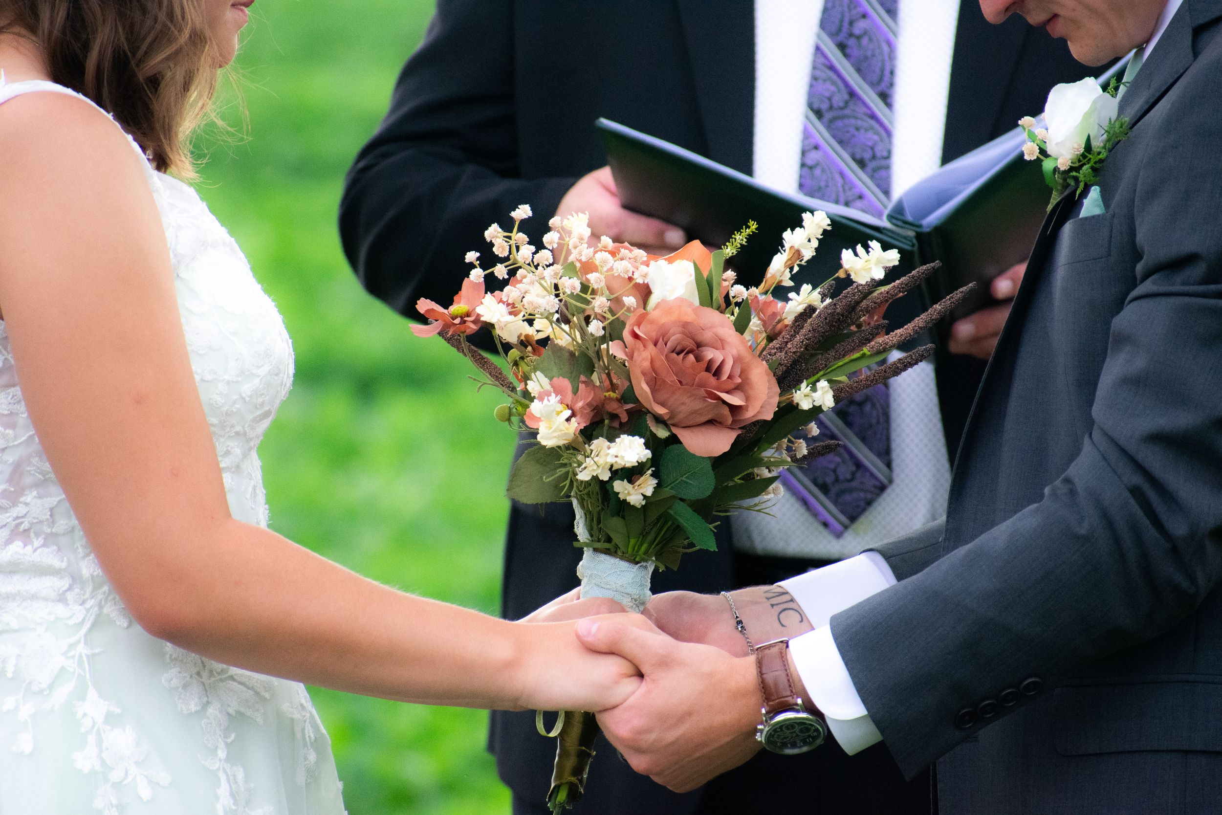 Close-up of hands exchanging rings during wedding ceremony with pink roses.