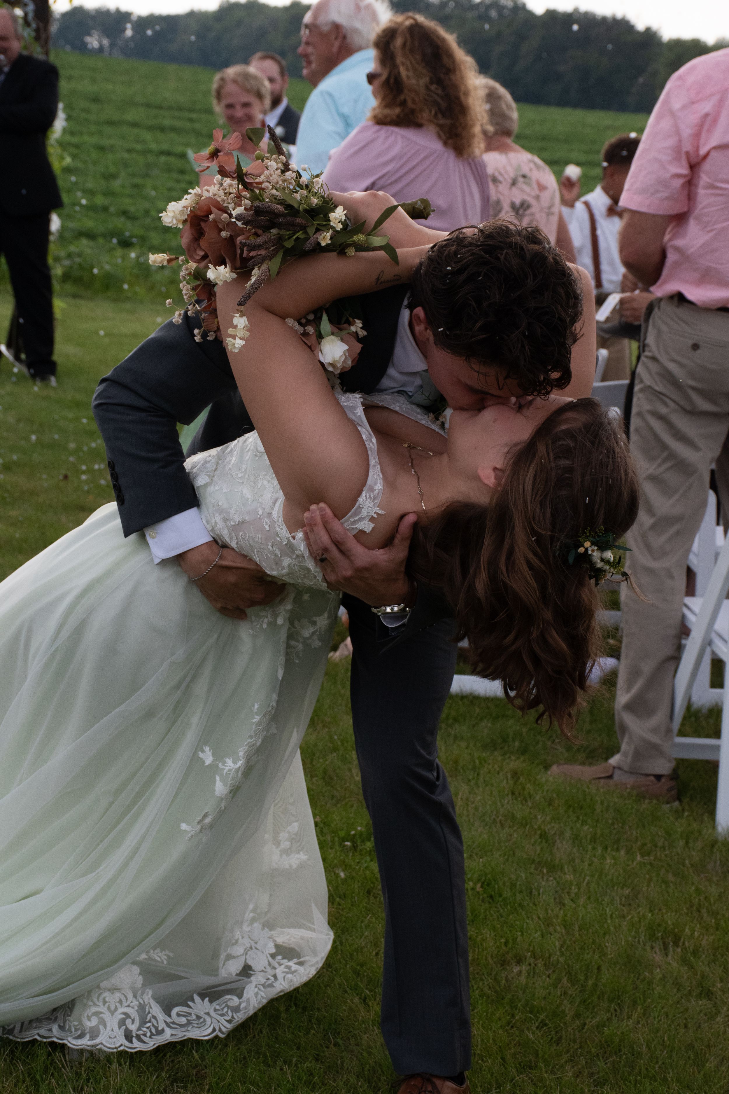 A romantic dip during a wedding ceremony on a green lawn with guests looking on.