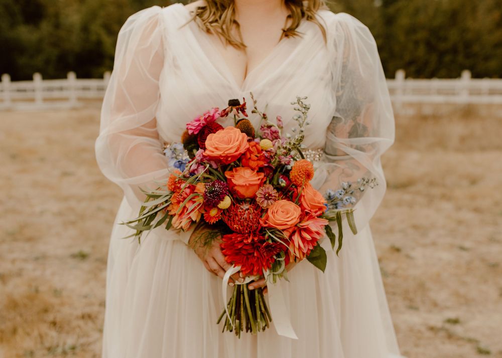 Vibrant coral and orange wedding bouquet held against cream colored dress.