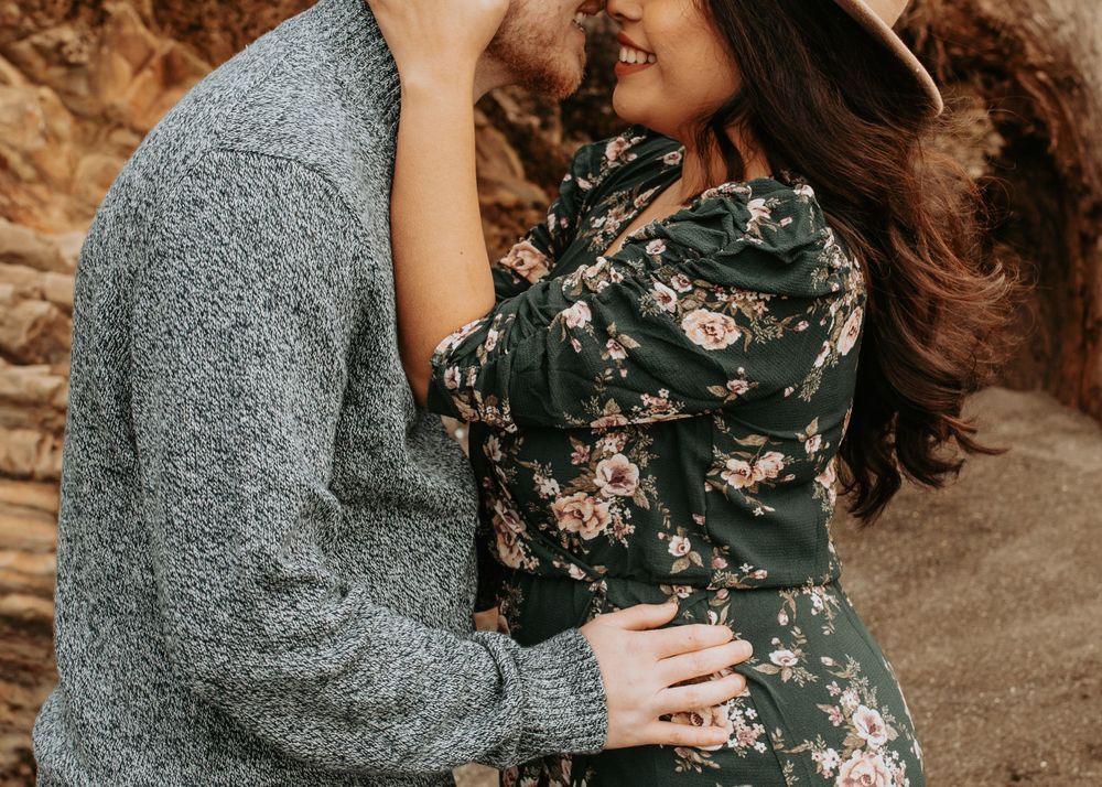 Intimate couples portrait against rocky backdrop with grey sweater and floral dress.